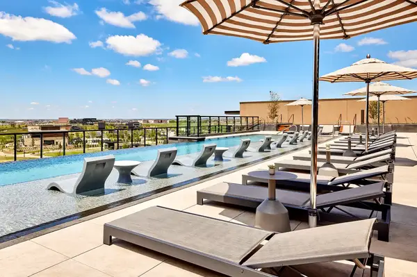 Outdoor pool area at a resort with loungers submerged in shallow water and seating under umbrellas