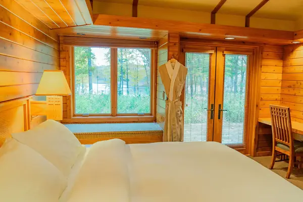 A cozy wooden cabin interior with a bed window overlooking trees and a bathrobe next to the door