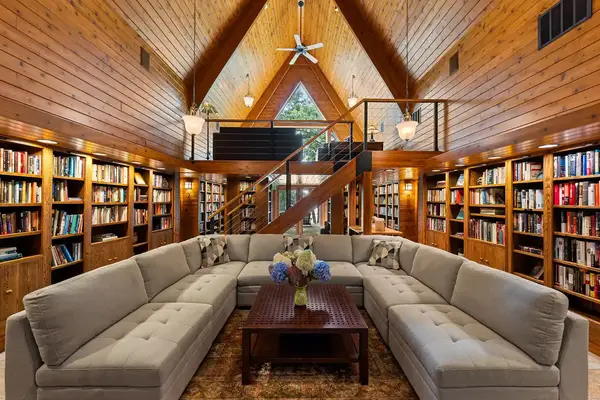 Large wooden interior with bookshelves a sectional sofa a wooden coffee table with flowers and a staircase leading to a loft area