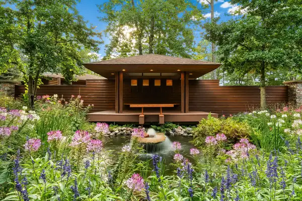 A view of a pavilion by a serene garden with a pond and surrounding flowers and trees