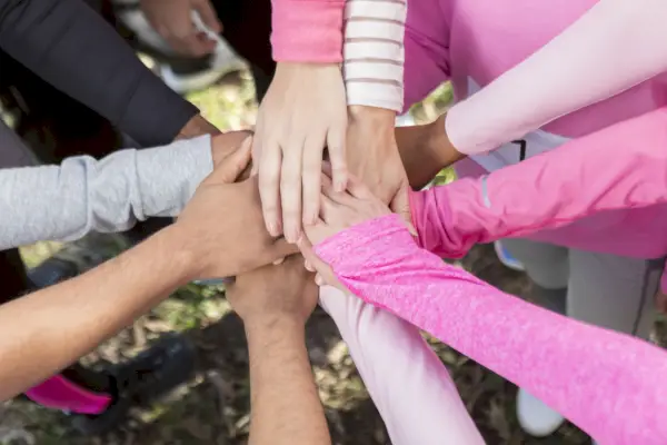 circle of people wearing pink shirts with their hands together in unity