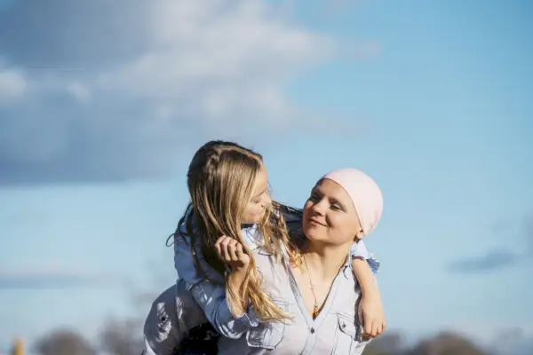 woman seen from chin to stomach holding out hands to make a heart shape to frame a pink ribbon on her white sweater