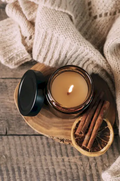candle in small amber glass jar with wooden wick on wooden stand on background copy space