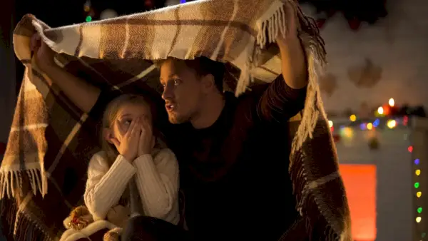 dad telling scary story for little girl covering her face with her hands and sitting under plaid blanket
