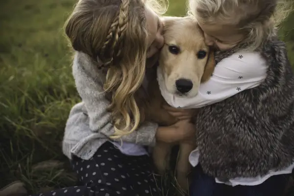 two young girls hugging pet dog, outdoors