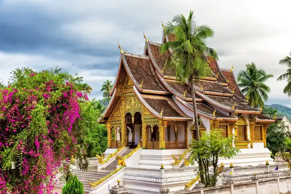 Traditional temple building in a landscaped area surrounded by trees and colorful flowers in Laos