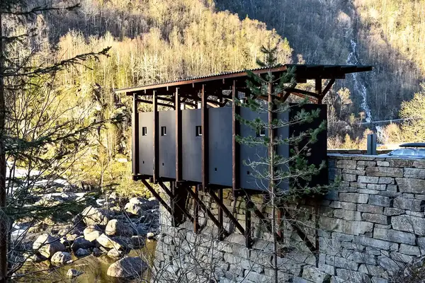 Modern rest area structure supported by stone and steel beams set in a wooded mountainous environment