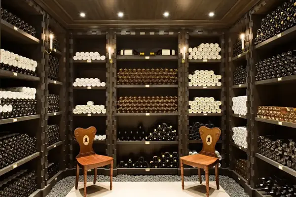 Interior of an organized wine cellar with shelves of wine bottles and two wooden chairs in the center