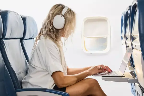 A person using a laptop on a plane while wearing the Sonos Ace Headphones