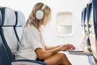 A person using a laptop on a plane while wearing the Sonos Ace Headphones