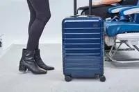 Person standing near Away The Carry-On bag alongside airplane seat