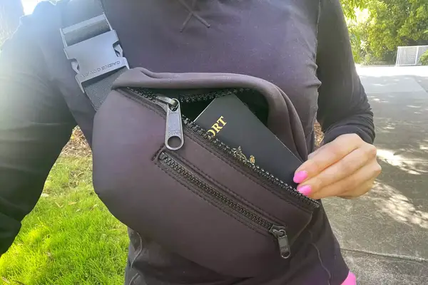 Hand removing a passport from the Dagne Dover Ace Fanny Pack being worn cross body