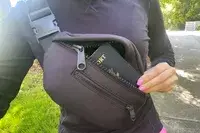 Hand removing a passport from the Dagne Dover Ace Fanny Pack being worn cross body