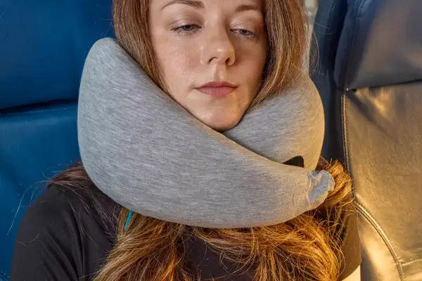 A person wearing the Ostrich Pillow Go Neck Pillow on a plane 