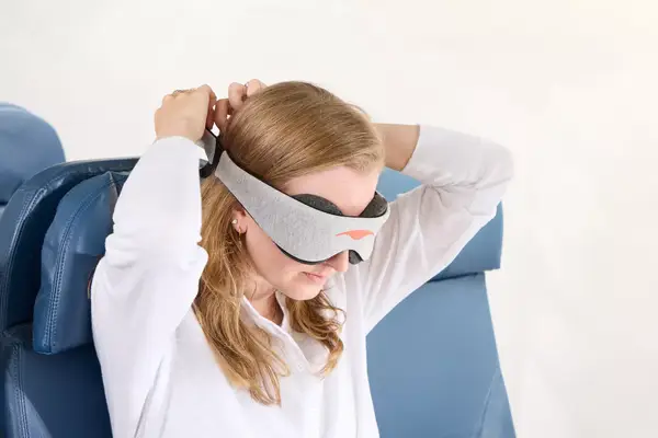 A person putting on the Manta Sleep Mask in an airplane seat