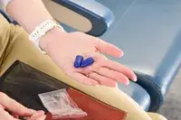 A hand holding purple ear plugs from the Manta Sleep Mask