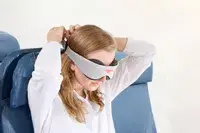 A person putting on the Manta Sleep Mask in an airplane seat