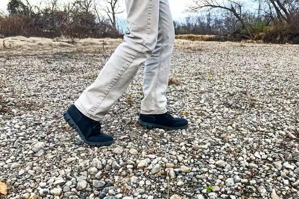 A person walks over pebbles while wearing the Bogs Arcata Urban Leather Mid Men