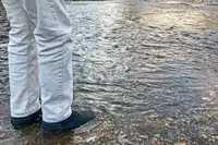 A person stands in water while wearing the Bogs Arcata Urban Leather Mid Men