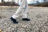 A person walks over pebbles while wearing the Bogs Arcata Urban Leather Mid Men