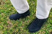 A person stands in grass while wearing the Bogs Arcata Urban Leather Mid Men