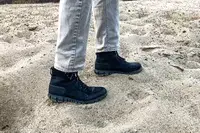 A person walks through sand while wearing the Bogs Arcata Urban Leather Mid Men
