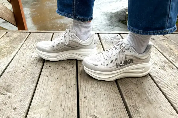 A close-up side-view of a person wearing the Hoka Bondi 9 sneakers on a wooden bridge