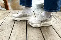 A close-up side-view of a person wearing the Hoka Bondi 9 sneakers on a wooden bridge