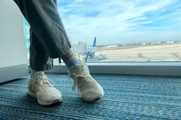 A person crossing their legs while wearing the Adidas Ultraboost 1.0 sneakers near an airport window 