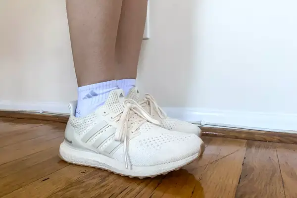 A close-up of the side-view of a person wearing the Adidas Ultraboost 1.0 sneakers on a wooden floor