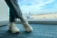 A person crossing their legs while wearing the Adidas Ultraboost 1.0 sneakers near an airport window 
