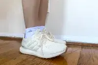 A close-up of the side-view of a person wearing the Adidas Ultraboost 1.0 sneakers on a wooden floor