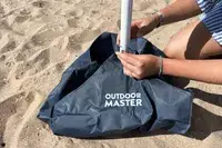 A person attaching the OutdoorMaster Beach Umbrella to the sand bag that holds it up