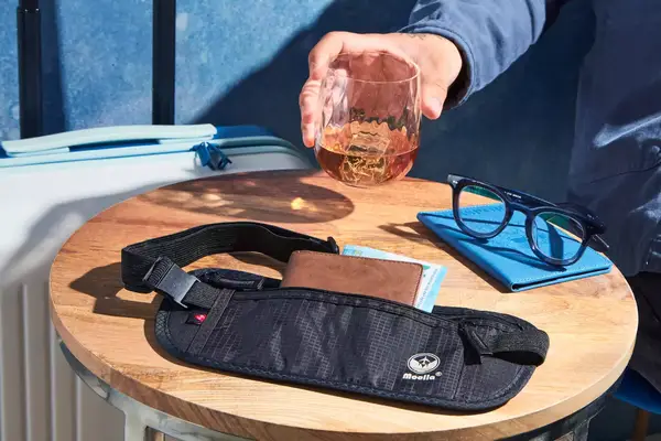 A person places a glass on a table alongside the Molarun Travel Money Belt