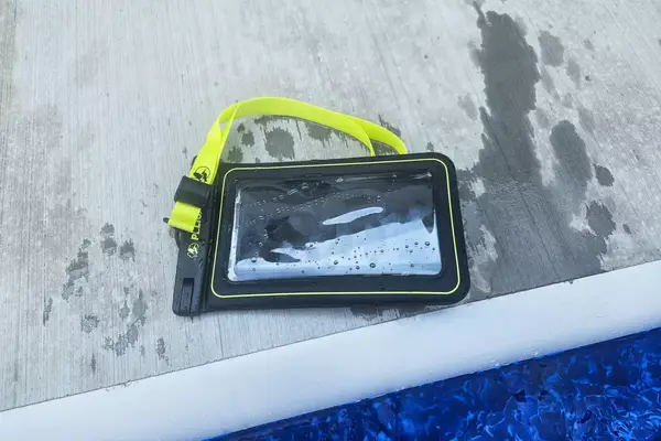 A wet Case-Mate Pelican Marine IP68 Waterproof Phone Pouch containing a phone on concrete near water