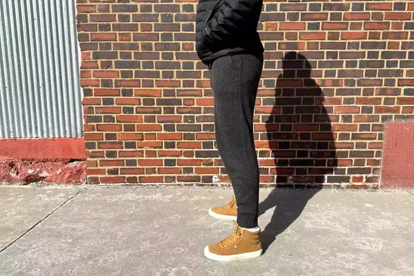 A person standing sideways by a brick wall while wearing the Quince Mongolian Cashmere Jogger