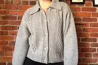 A person wearing the Quince Australian Merino Wool Collared Cable Cardigan standing in front of a brick wall