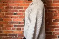 A person wearing the Quince Australian Merino Wool Collared Cable Cardigan standing in front of a brick wall