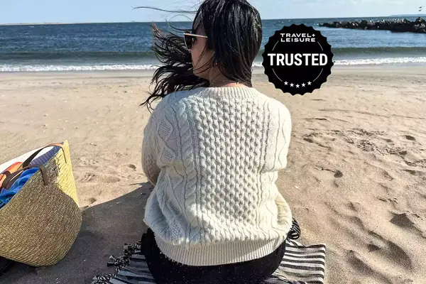 A person wearing the Buck Mason Highland Alpaca Cable Crew Sweater on a beach