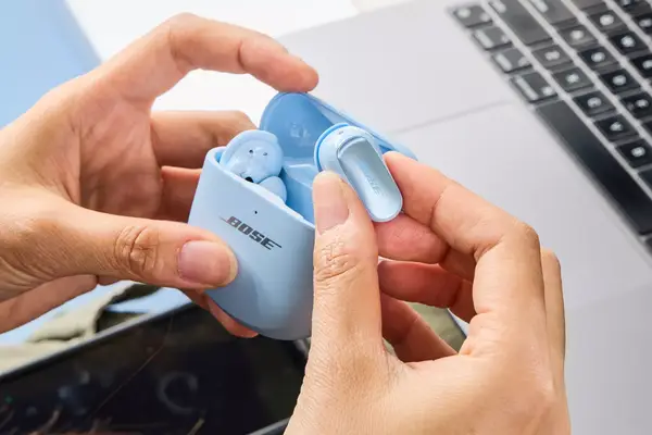 A person removing a Bose QuietComfort Ultra Earbud from its case over a laptop