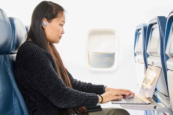 A person sitting on a plane on their laptop while wearing the Bose QuietComfort Ultra Earbuds