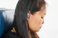 A close-up from the side of a person wearing the Bose QuietComfort Ultra Earbuds while sitting on a plane seat