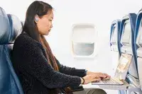 A person sitting on a plane on their laptop while wearing the Bose QuietComfort Ultra Earbuds