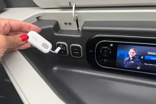 A hand plugging the Twelve South AirFly SE into a headphone port on an airplane