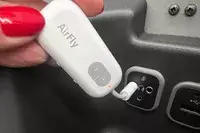 A hand plugging the Twelve South AirFly SE into a headphone port on an airplane