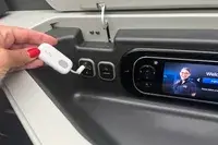 A hand plugging the Twelve South AirFly SE into a headphone port on an airplane