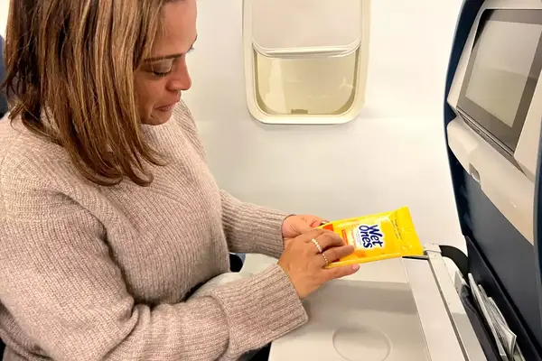 A person opening a Wet Ones Antibacterial Hand Wipes Travel Pack on a plane