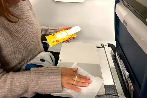 a person using a Wet Ones Antibacterial Hand Wipe to clean the tray table on a plane