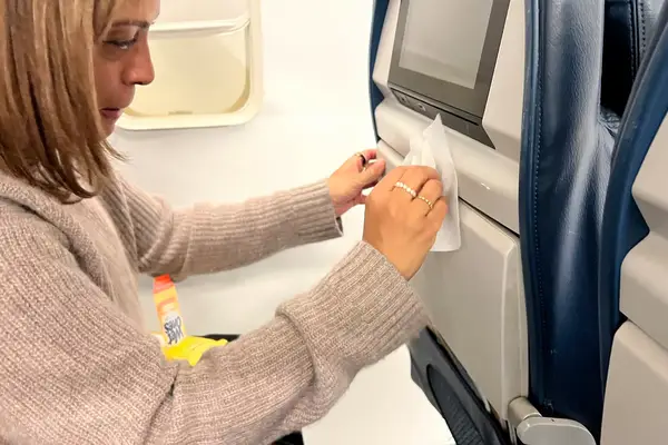 A person using a Wet Ones Antibacterial Hand Wipe to wipe down the tray table on a plane