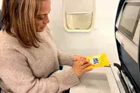 A person opening a Wet Ones Antibacterial Hand Wipes Travel Pack on a plane